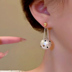 Close-up of polka dot pearl ball drop earring with gold stud, worn on ear