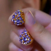 Pair of gold-tone purple rhinestone triangular stud earrings held in hand