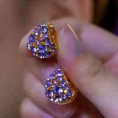 Pair of gold-tone purple rhinestone triangular stud earrings held in hand