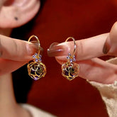 Pair of Hollow Gold Purple Rose Rhinestone Dangle Earrings Held in Hand