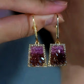Pair of gold gradient purple-brown crystal trapezoid drop earrings held in fingers
