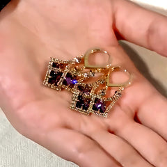 Gold tone purple square crystal drop dangle earrings held in hand