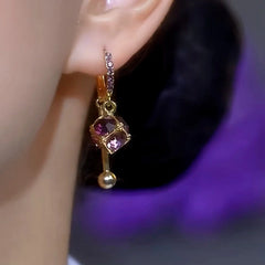 Gold purple cubic crystal dangle huggie hoop earring worn on ear, alternate side view