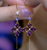 Purple crystal flower gold dangle earrings, pair held between fingers