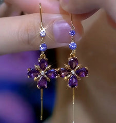 Purple crystal flower gold dangle earrings, pair held between fingers