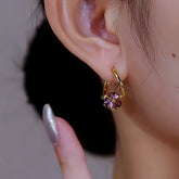Gold huggie hoop earring with purple cubic gem worn on woman's right ear