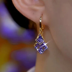 Gold purple crystal double rhombus drop earring worn on ear, floral background