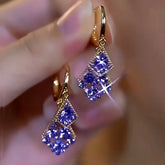 Pair of gold purple crystal double rhombus huggie drop earrings held in hand