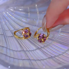 Pair of gold purple cubic gem huggie hoop earrings on iridescent surface