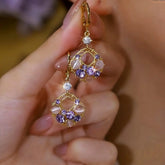 Pair of vintage gold purple crystal cat's eye dangle hoop earrings held in hand