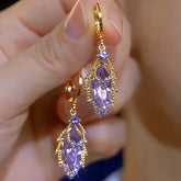 Pair of gold purple crystal leaf dangle hoop earrings held in hand