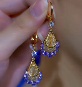 Pair of gold purple crystal teardrop dangle earrings held between fingers, close-up