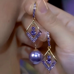Pair of gold tone purple rhinestone rhombus pearl drop earrings held in hand