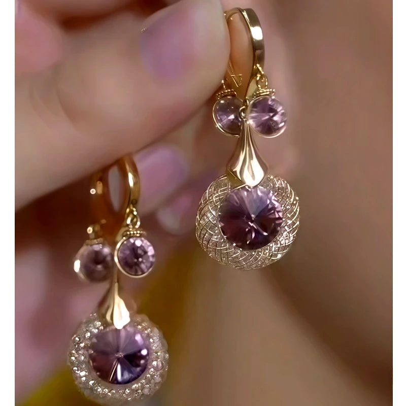 Pair of gold purple crystal woven drop earrings held in hand