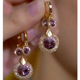 Pair of gold purple crystal woven drop earrings held in hand