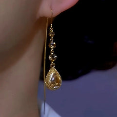 Women's gold teardrop crystal long dangle earring worn on ear, side close-up