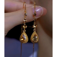 Pair of women's gold champagne crystal teardrop long dangle earrings held by hand