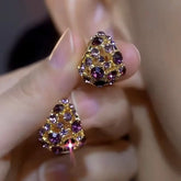 Pair of gold-toned purple rhinestone triangular stud earrings held in hand