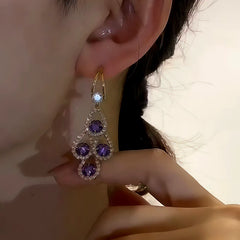 Close-up of purple crystal gold dangle earring on female ear