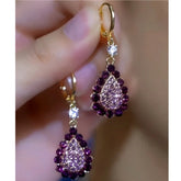 Hand holding a pair of women's purple teardrop rhinestone dangle earrings with gold hoops