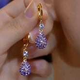 Pair of women's gold purple teardrop pave crystal dangle hoop earrings held in hand