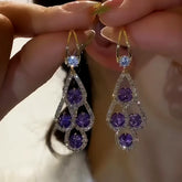Pair of gold hook purple crystal teardrop drop dangle earrings held in hands