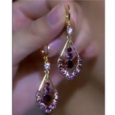 Pair of gold purple crystal teardrop dangle earrings held in hand