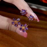 Purple cubic zirconia flower gold hoop earrings held between manicured fingers