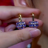 Pair of gold purple crystal ball drop hoop earrings held in hand, front close-up