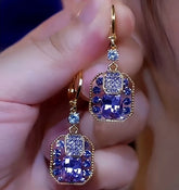 Pair of purple blue crystal gold-tone drop earrings held in hand