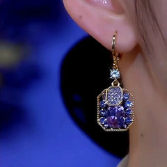 Purple blue crystal gold-tone drop earring worn on left ear