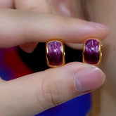 Pair of gold-tone purple gemstone huggie earrings held between fingers