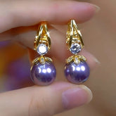Pair of gold purple pearl drop earrings with crystal accents, held between fingers