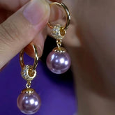 Pair of gold hoop purple pearl drop earrings with crystal accents held in hand