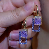 Pair of women's gold purple and blue square crystal drop earrings held in hand
