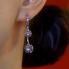 Close-up side view of purple crystal drop hoop earring worn on ear