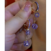Hand holding pair of gold-tone purple crystal dangling hoop earrings