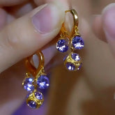 Pair of gold purple crystal dangle drop earrings held between fingertips