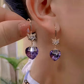 Women's rose gold fox hook earrings with purple heart crystal drop, worn and held by hand