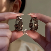 Pair of sparkly smoky brown crystal huggie hoop earrings held between fingers