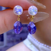 Pair of gold tone iridescent pearl purple faceted teardrop crystal drop earrings held by hand