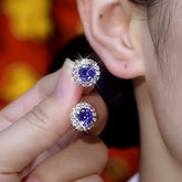 Pair of round purple gemstone halo stud earrings held near ear