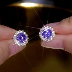 Sparkling purple center stone halo stud earrings held between fingertips
