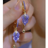 Pair of purple rhinestone leaf gold hoop drop earrings held in hand