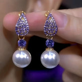 Pair of purple teardrop rhinestone pearl drop earrings held between fingers