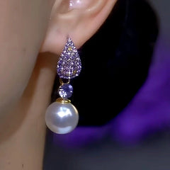 Purple rhinestone pearl drop earring worn on a person's ear
