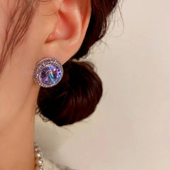 Closeup of purple-blue round crystal halo stud earring on earlobe