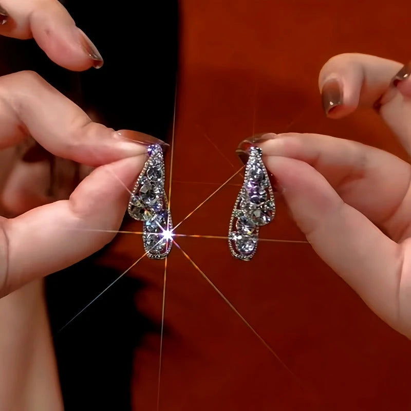 Pair of silver teardrop crystal drop earrings held by manicured hands