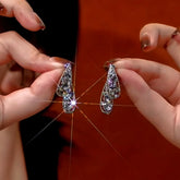 Pair of silver teardrop crystal drop earrings held by manicured hands