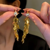Pair of gold rhinestone rabbit leaf tassel dangle earrings held in hands